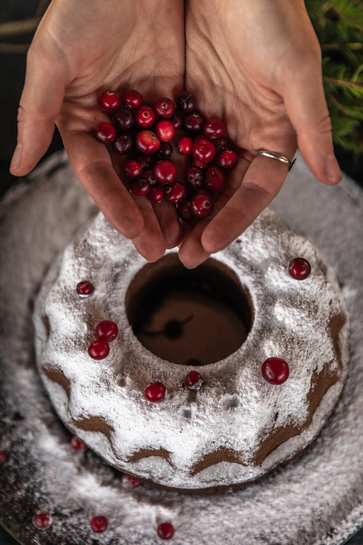 Person Holding Cranberries Near A Cake