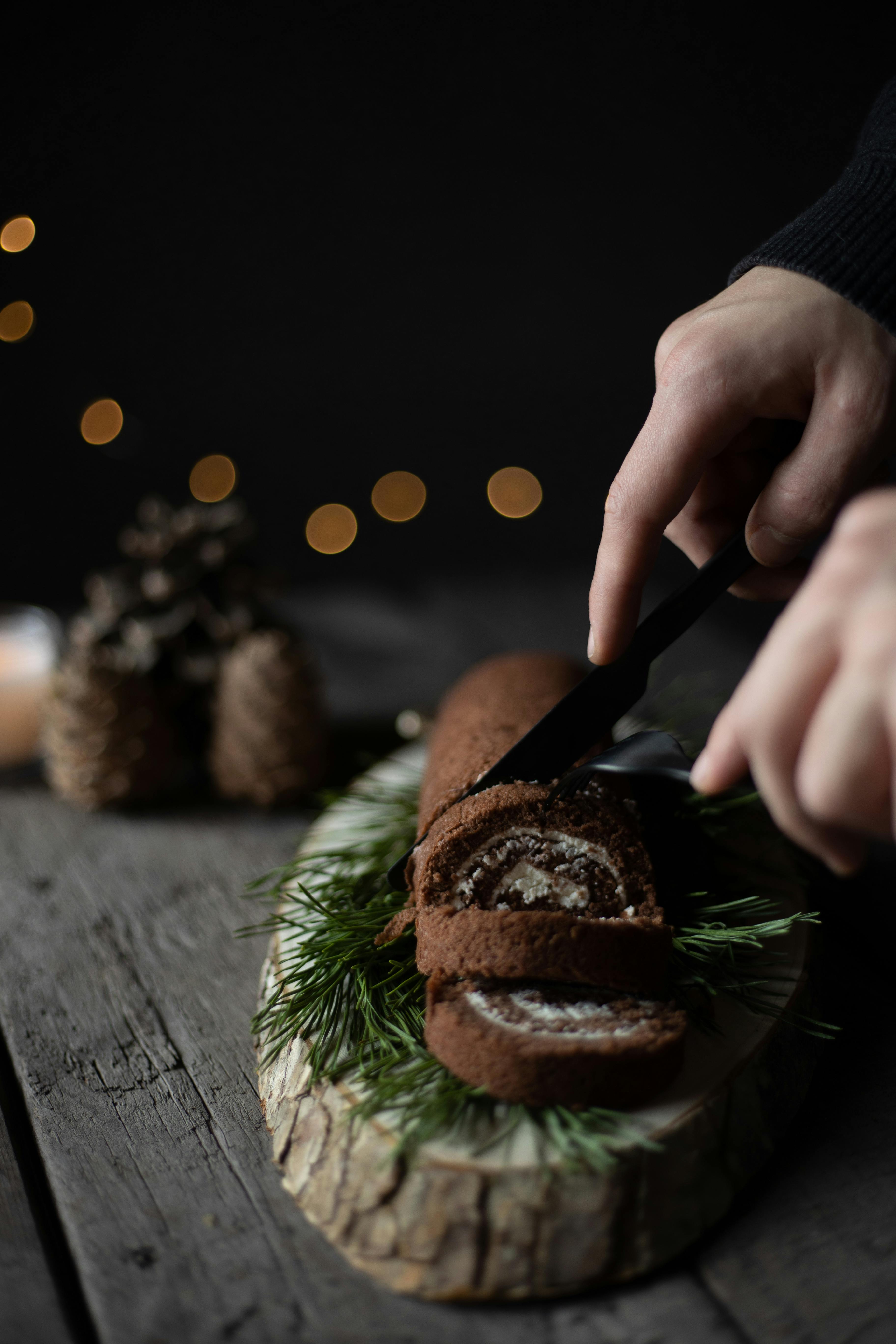 在带有节日装饰的木砧板上，巧克力圣诞原木被切片的特写镜头