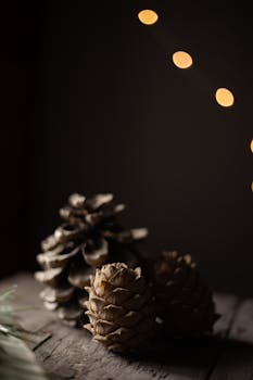 Close-up of pine cones on wooden surface with warm, blurred lights creating a cozy winter ambiance.