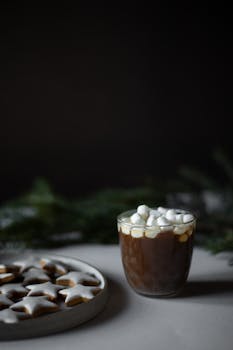 Cozy hot chocolate topped with marshmallows next to plate of gingerbread cookies.