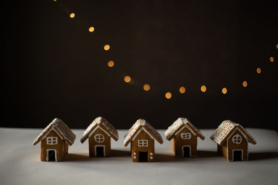 Five gingerbread houses with icing details, set against soft golden bokeh lights creating a cozy holiday feel.