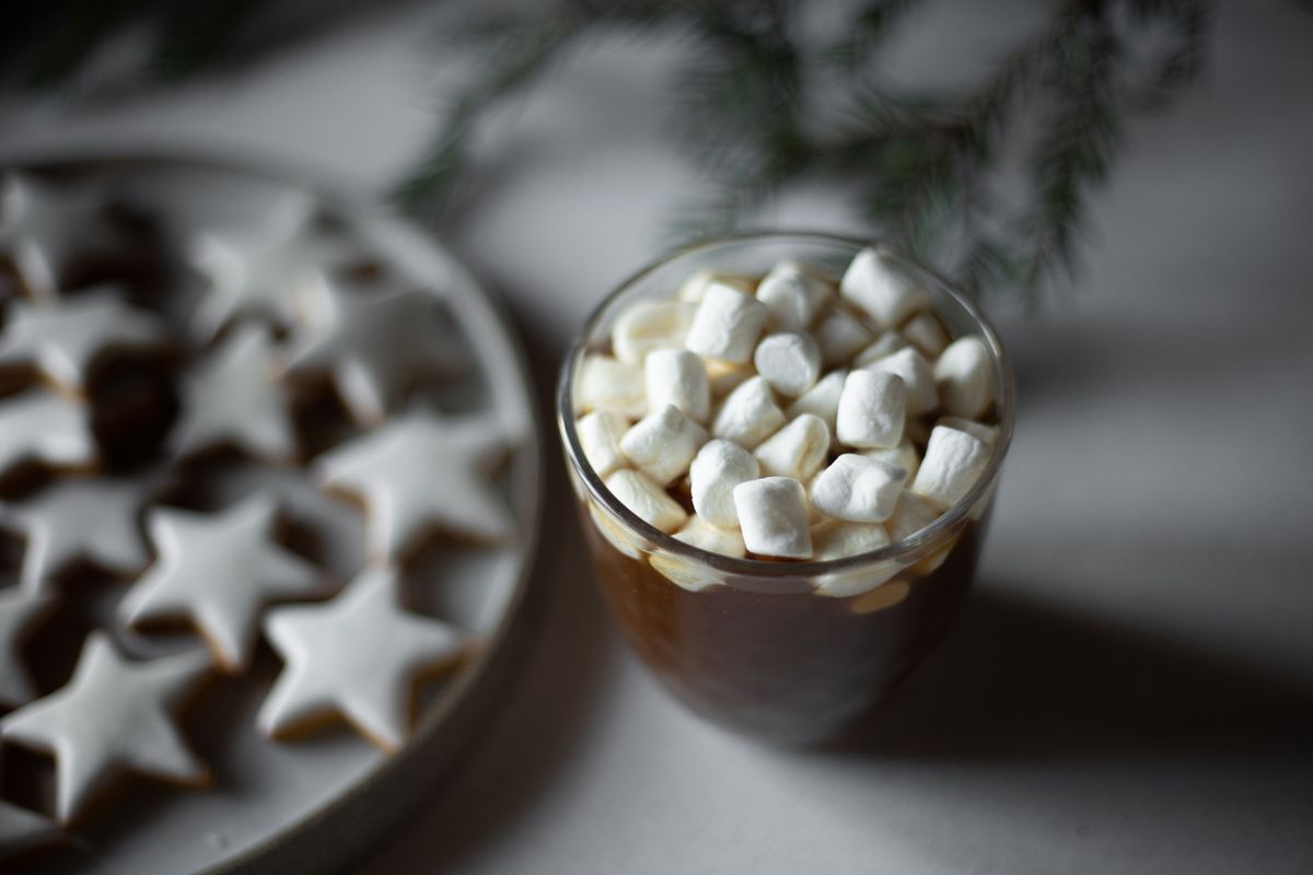 Warm hot chocolate topped with marshmallows beside star-shaped cookies, perfect for winter cozy vibes.
