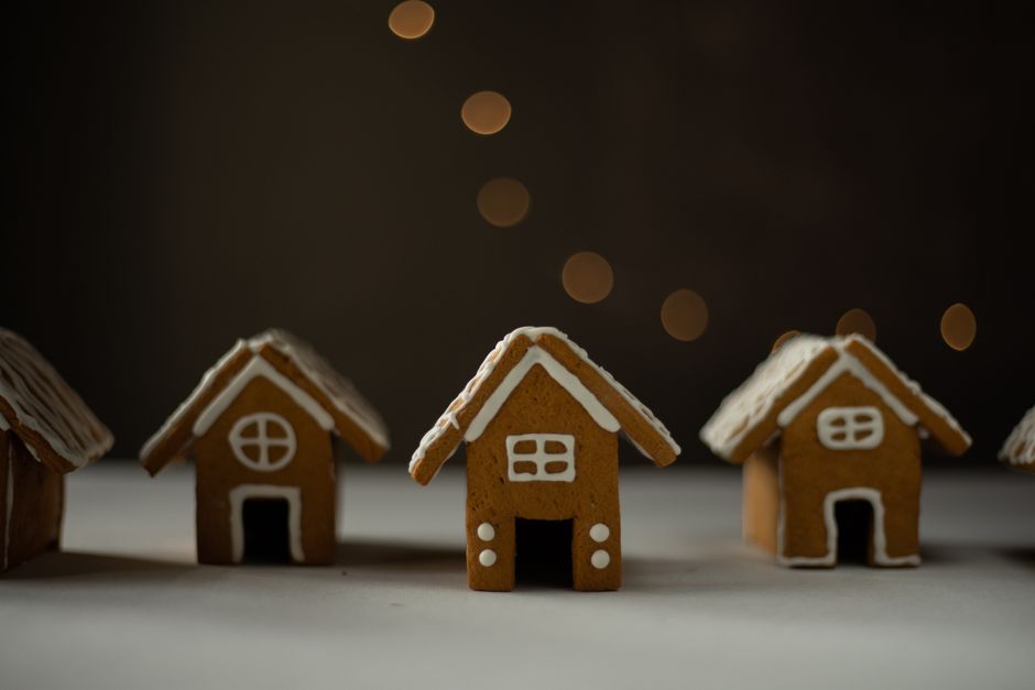 A finished gingerbread house with royal icing snow on the roofline, gumdrops along the roof edge, and a candy cane border around the base.