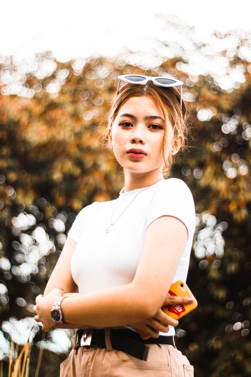 Free Portrait of a stylish woman outdoors with fall leaves background, exuding confidence in a fashionable outfit. Stock Photo