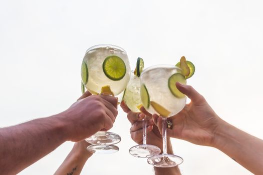 Friends toasting with gin cocktails garnished with lime and cucumber outdoors.