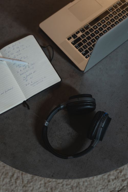 Free A cozy workspace featuring a laptop, headphones, and a notebook with pen on a round table. Stock Photo