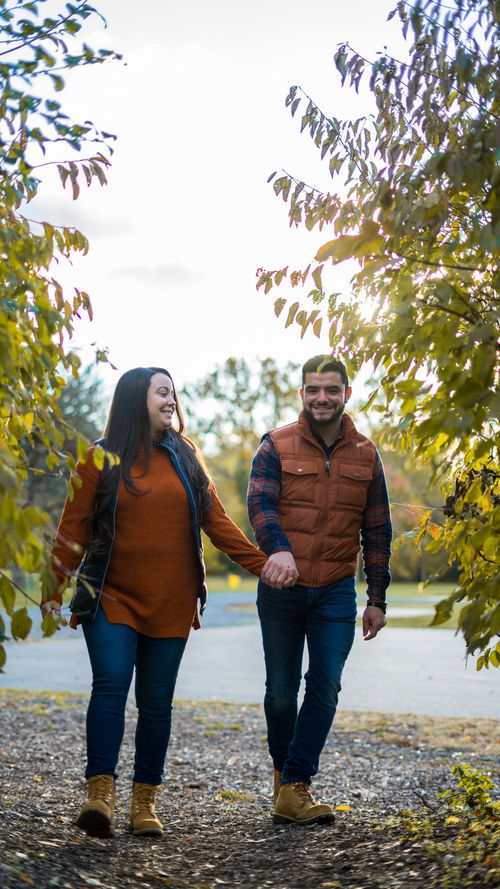 Free A joyful couple holding hands while walking through a vibrant autumn park. Stock Photo