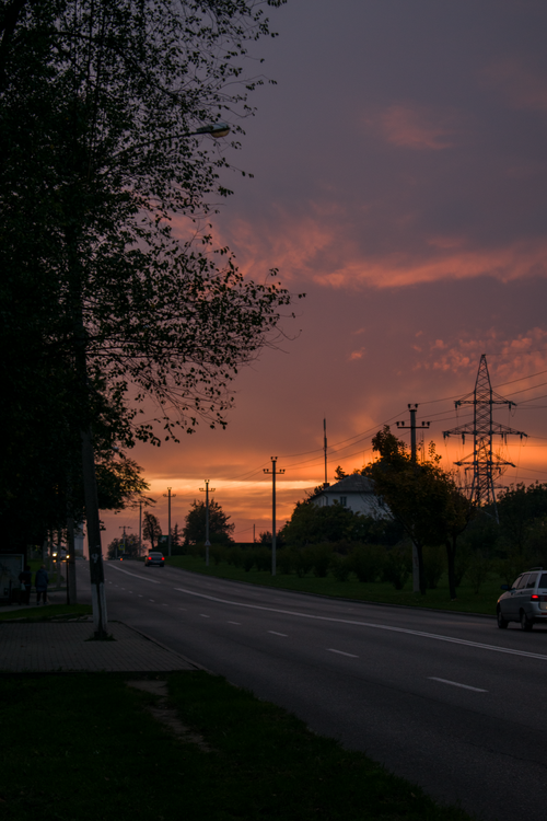 Free A peaceful road at sunset with silhouetted trees and electric poles against a vibrant sky. Stock Photo
