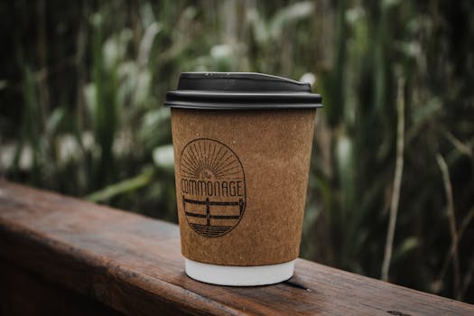 A compostable coffee cup on a wooden surface, surrounded by greenery, emphasizing sustainability.