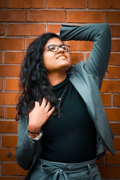 Free Confident woman in blazer posing against a brick wall outdoors, exuding a stylish and carefree vibe. Stock Photo