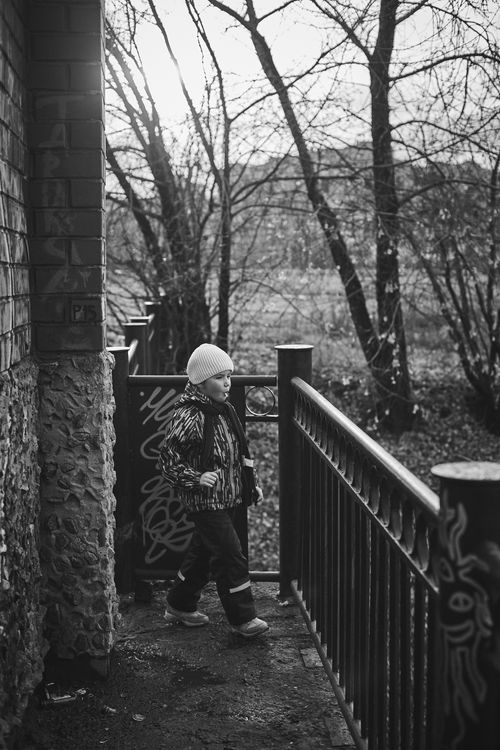 Free Black and white image of a child walking by a railing in a wooded area. Stock Photo