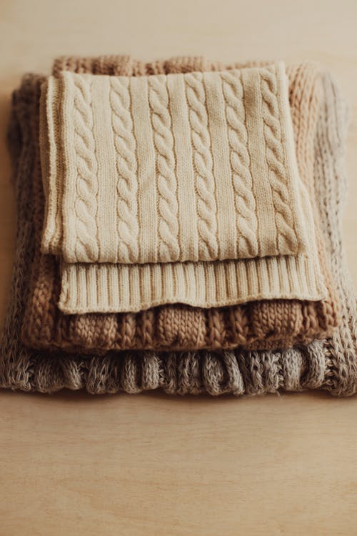 High angle of warm knitted scarfs of various shades of beige color on wooden table