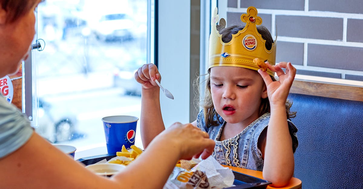 A child wearing a paper crown eats with mother at a fast food restaurant.