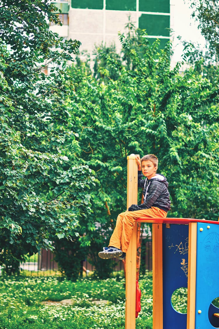 A Boy Wearing A Black Jacket Sitting On The Playground Equipment