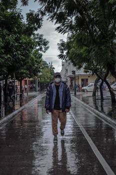 A man walks along a wet street in a rainy urban area during winter.