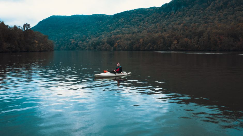 Kayaker glides on peaceful lake surrounded by mountain landscape in daytime.
