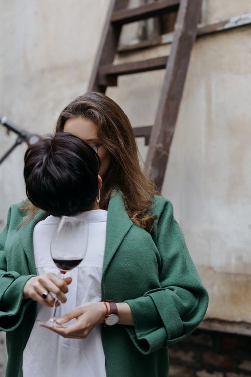Free Intimate moment of LGBTQ couple kissing while holding a glass of red wine outdoors. Stock Photo