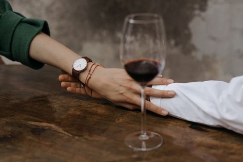 Free A close-up of two hands holding across a table with a glass of red wine, capturing a moment of intimacy. Stock Photo