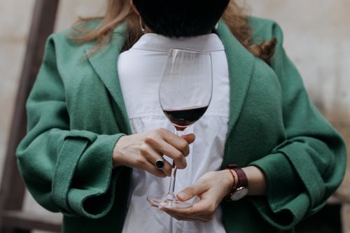 Free A woman in a green coat holds a wine glass filled with red wine, showcasing elegance and style. Stock Photo