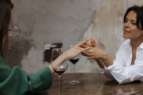 Free Two women share an intimate moment over red wine, holding hands in a cozy setting. Stock Photo