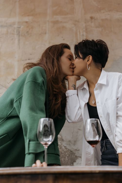 Free A loving moment between a couple sharing a kiss with wine glasses in an intimate setting. Stock Photo