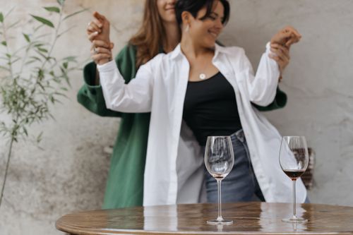 Free Joyful couple dancing indoors with wine glasses on a table, capturing romance. Stock Photo