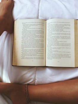 A cozy overhead view of an open book and resting legs on a bed, creating a relaxing mood.