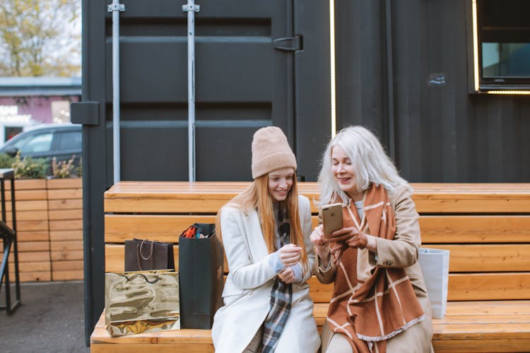 Two Women Sitting On Brown Wooden Bench