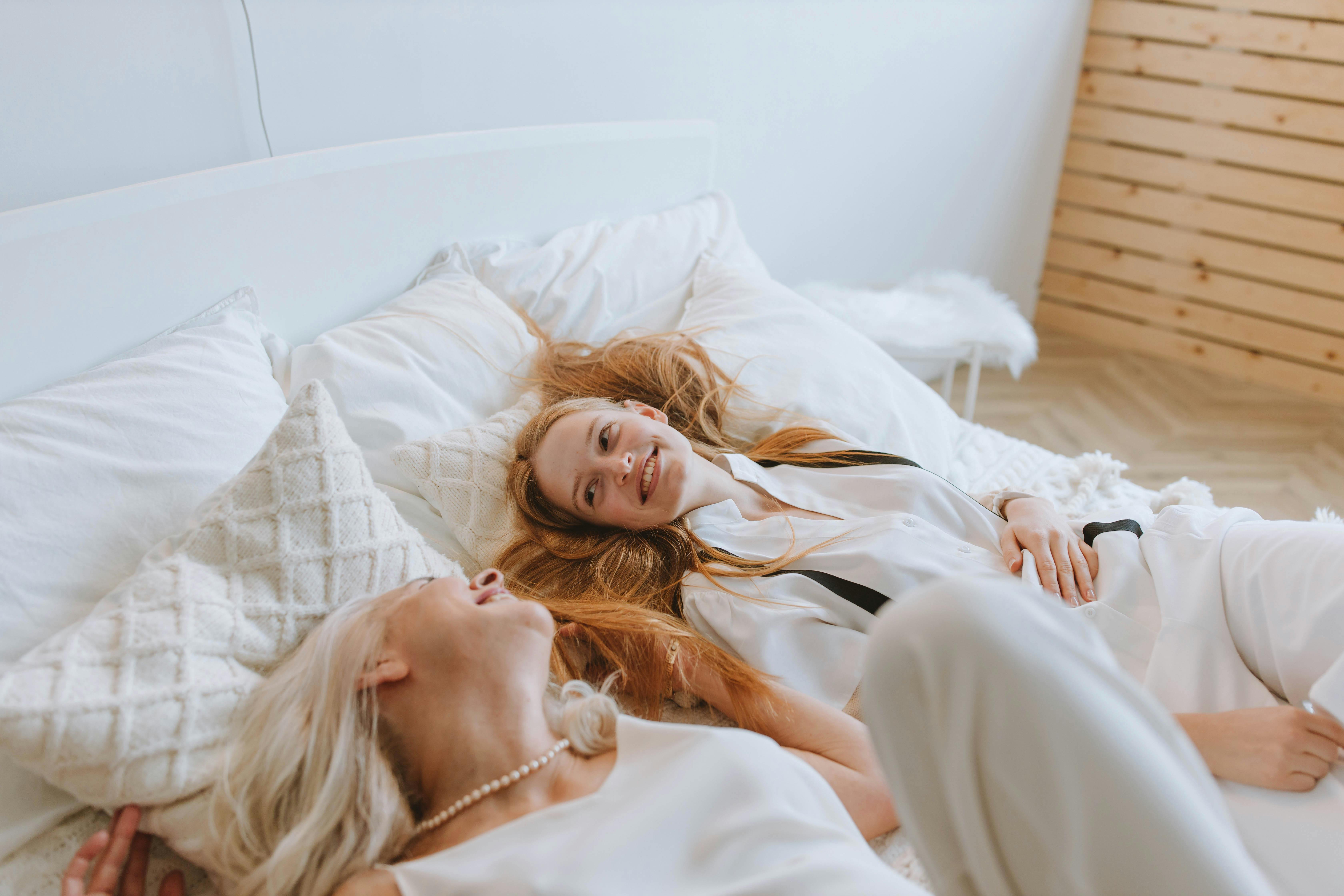 A grandmother and granddaughter share a joyful moment in a bright, cozy bedroom, filled with warmth and connection.