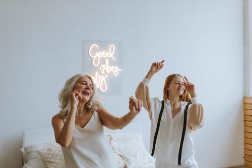 Free A grandmother and granddaughter dancing joyfully in a cozy room with a 'Good Vibes Only' sign. Stock Photo