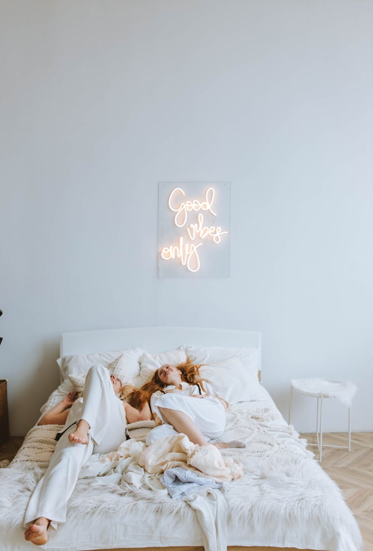 Woman Lying On White Bed Under Neon Sign