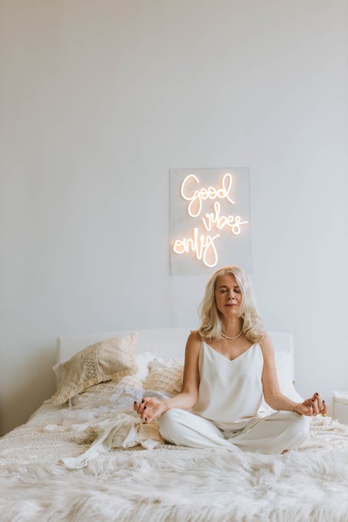 Woman in White Strap Top Sitting on Bed in Lotus Pose with Eyes Closed