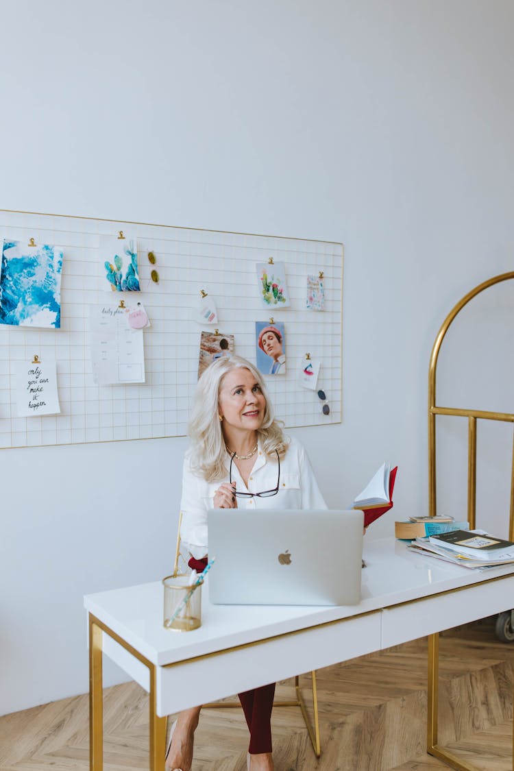 Woman In White Shirt Holding Eyeglasses While Sitting On Chair In Front Of White Laptop