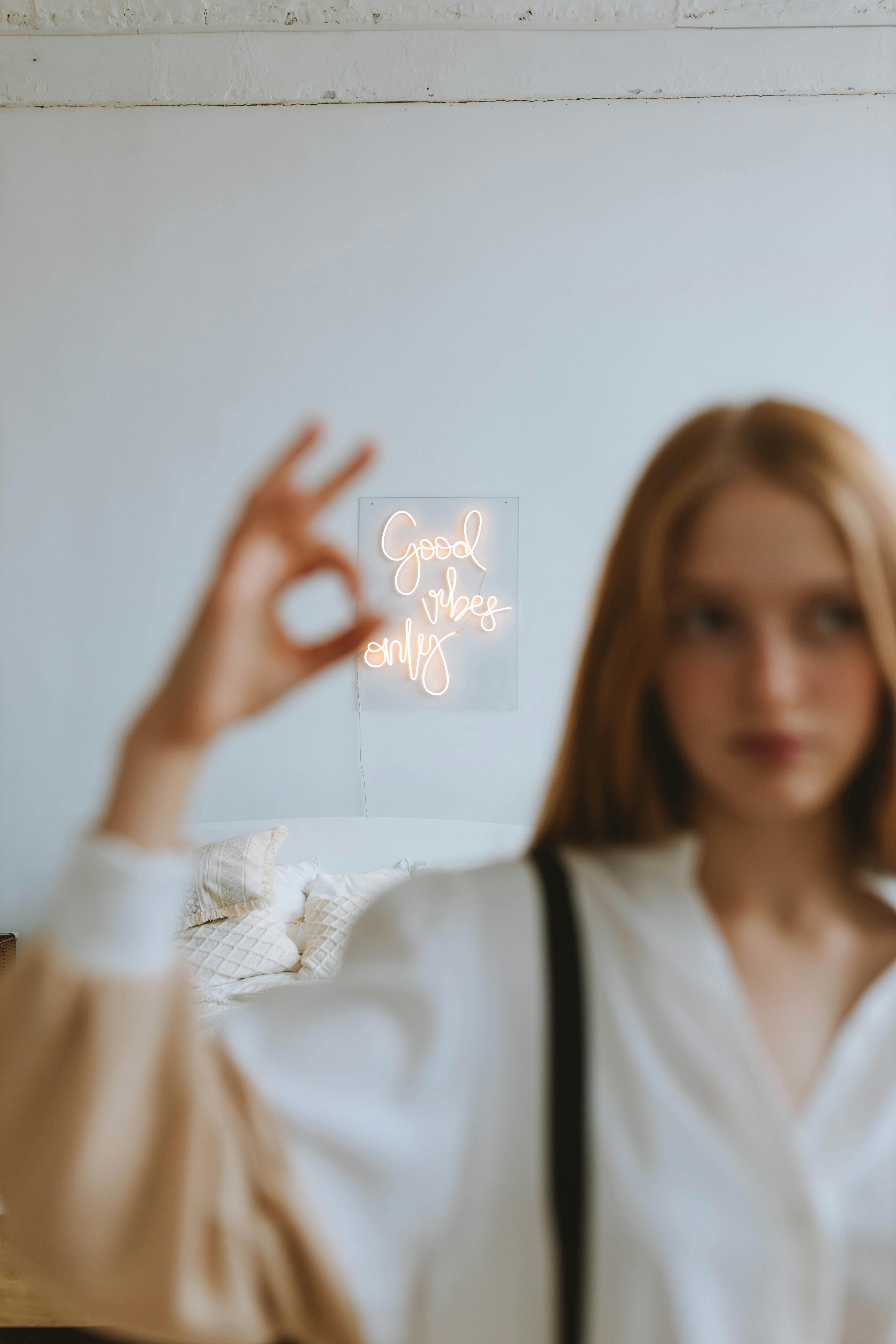 Free Neon Sigh Behind Woman in White Shirt Showing Hand Gesture Vulnerability and Authenticity