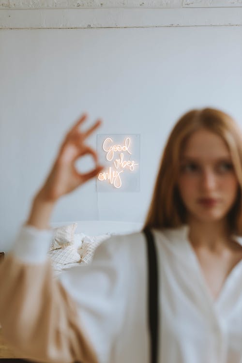 Free Neon Sigh Behind Woman in White Shirt Showing Hand Gesture Stock Photo