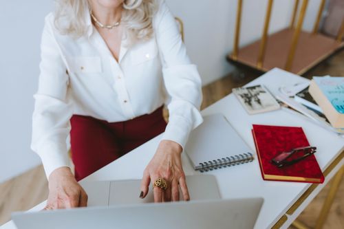 Free A senior woman using a laptop at a desk with books and a notebook, representing remote work. Stock Photo