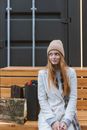 一位穿着时尚的年轻女子坐在户外的长凳上，旁边放着购物袋