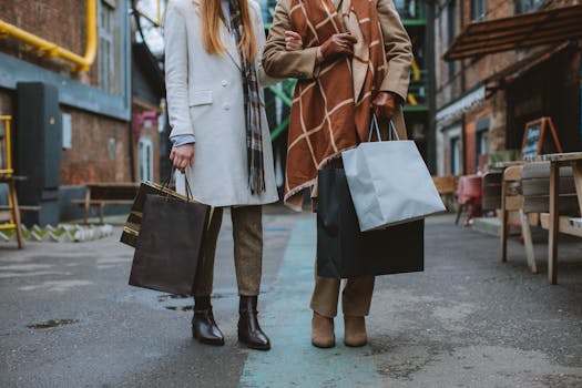 Two fashionable women walking and shopping on a city street with bags, wearing coats and boots in a winter setting.