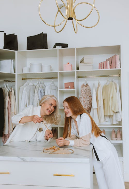 Free Woman in White Shirt Showing Golden Necklace to a Girl in White Clothes Beside Stock Photo