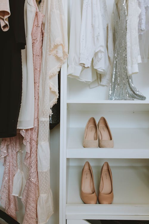 Beige Shoes on White Wooden Shelf Under Clothes 