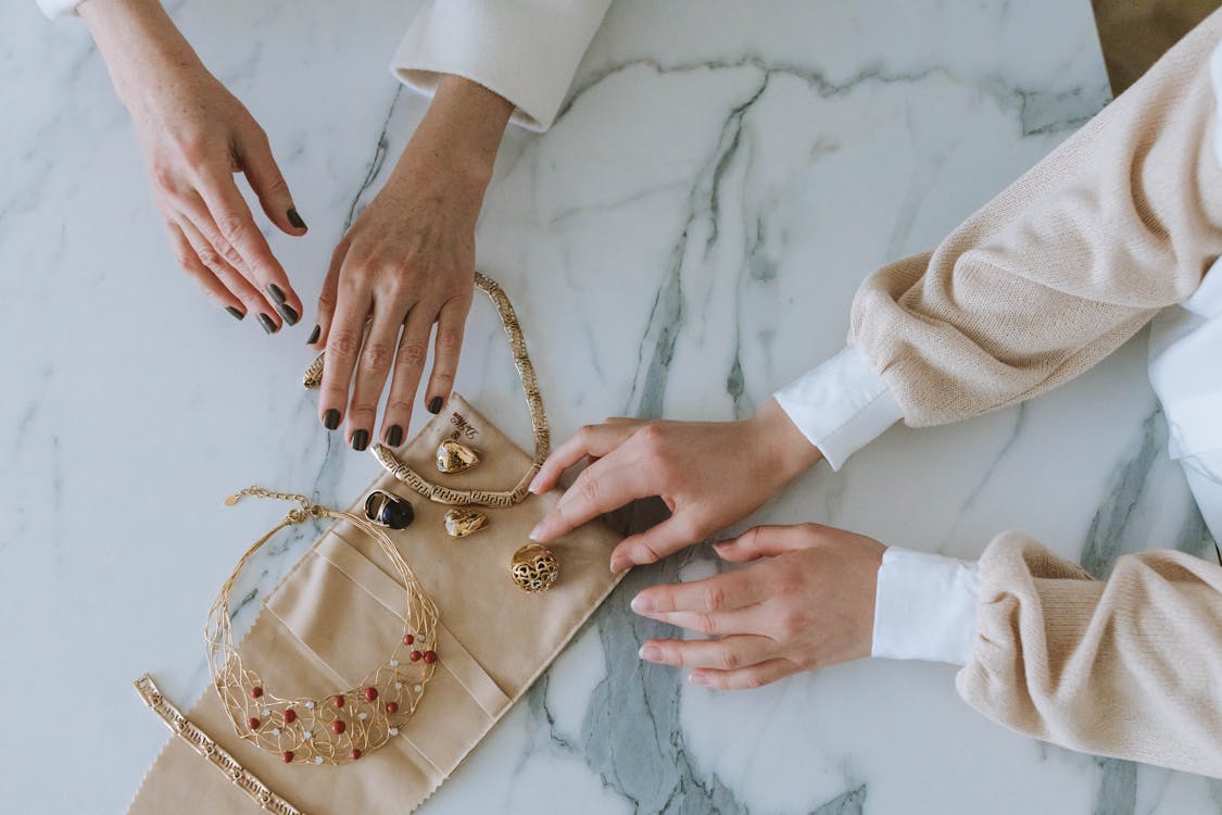 Free Two Women Touching Golden Jewelry on Marble Floor Stock Photo