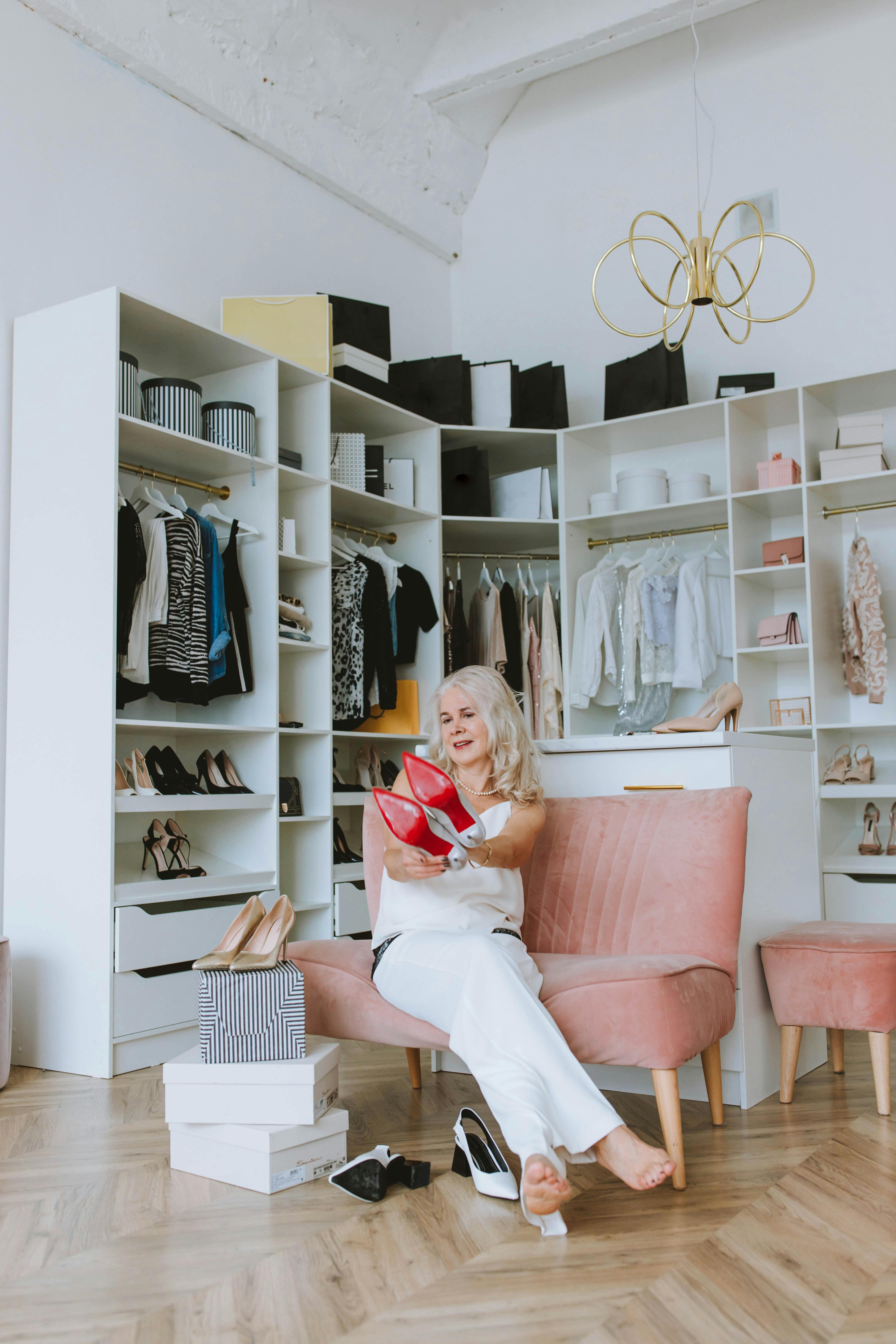 年长的女性在家里，周围摆满了衣服和鞋子，享受着时尚的衣柜