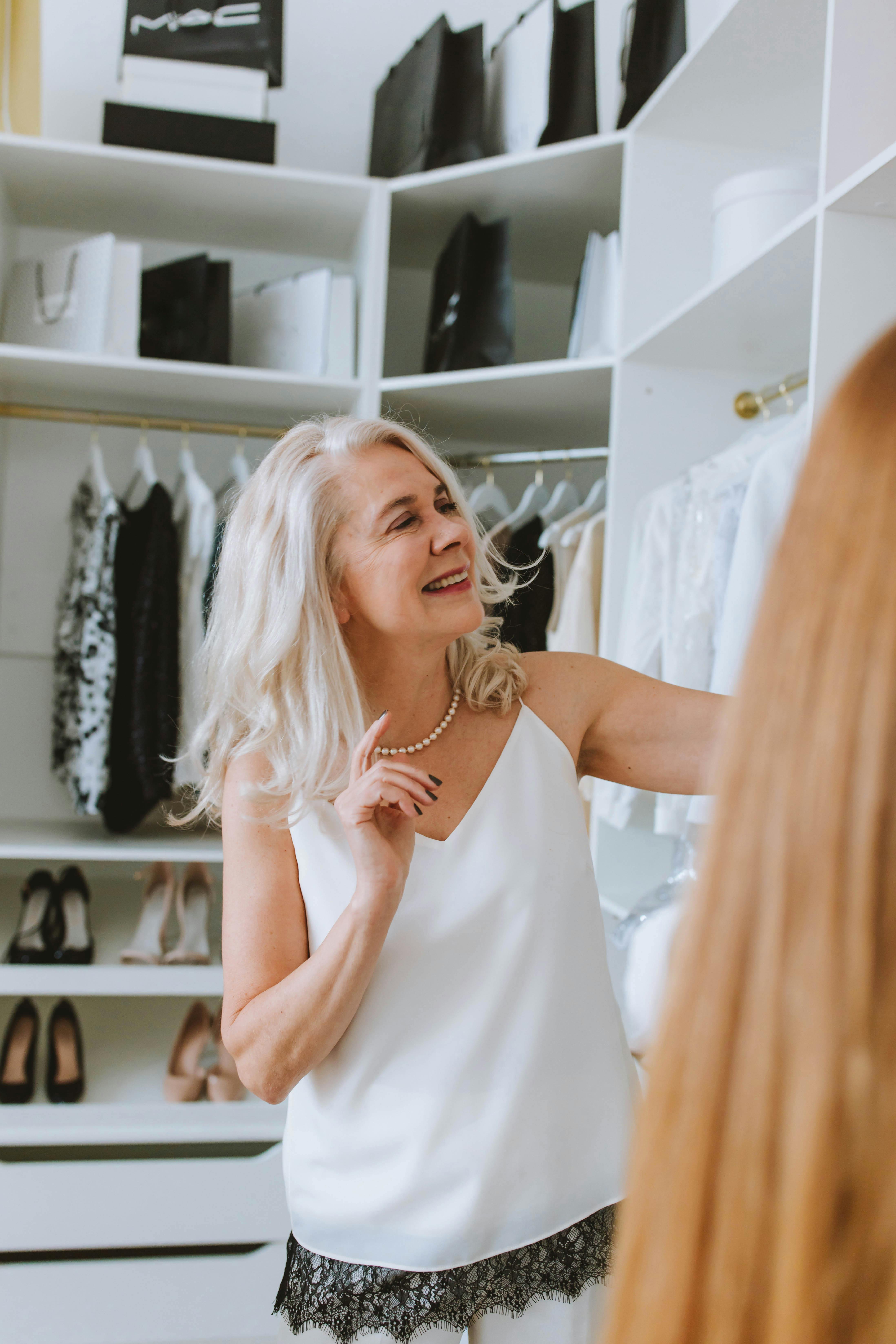 Senior woman with white hair smiling while selecting clothes in a walk-in closet.