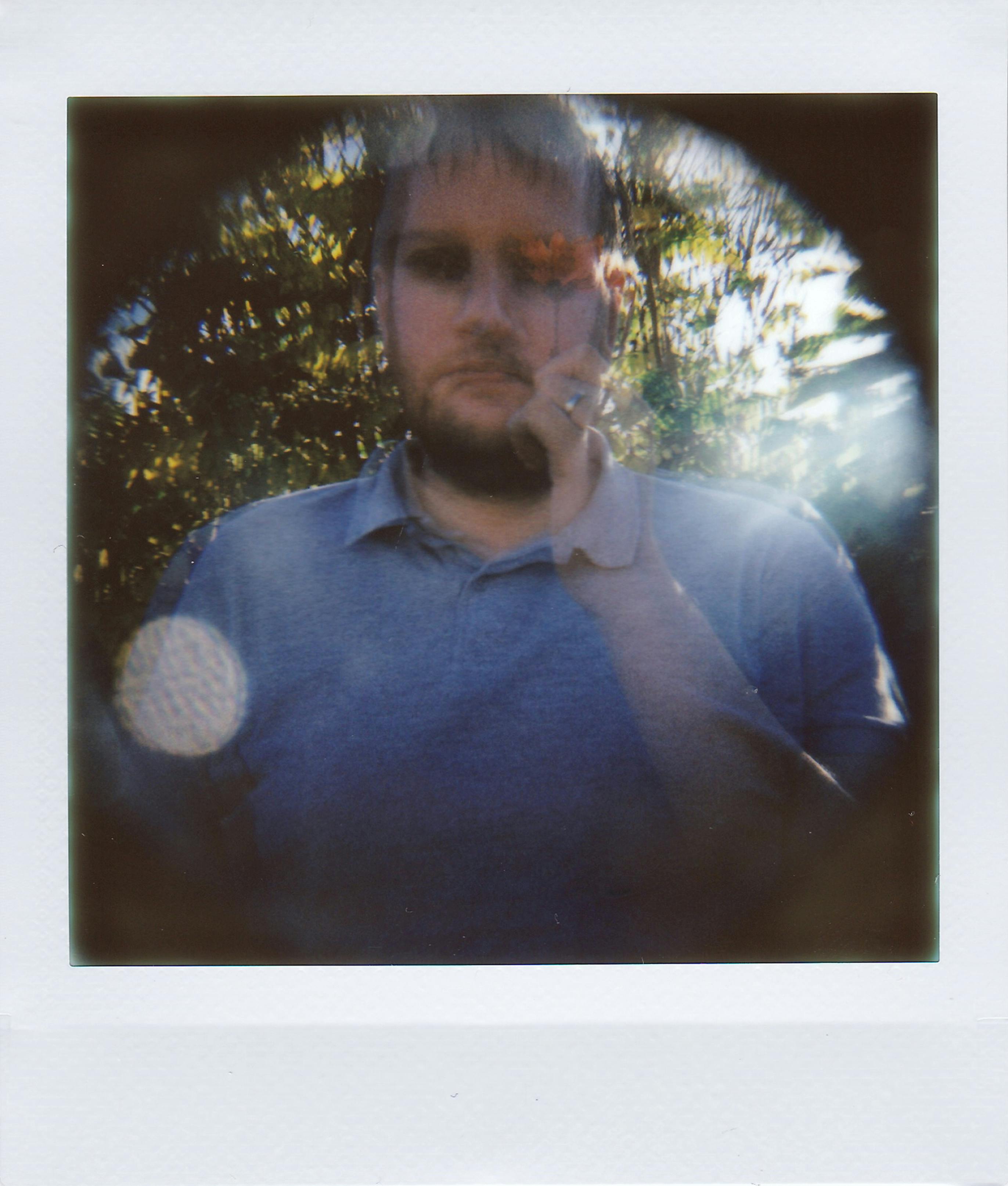 A warm vintage-style Polaroid portrait of a man in a sunlit outdoor setting, captured in a dreamy blurred effect.