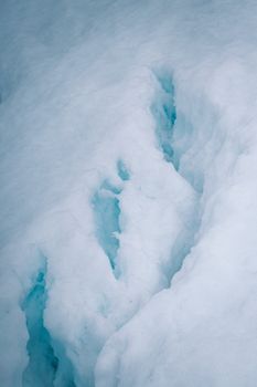 Snowy ice surface with visible crevices showing shades of blue in a winter setting.