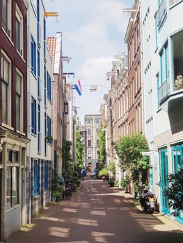 Cozy narrow street in Amsterdam featuring Dutch-style buildings and a flag on a sunny day.