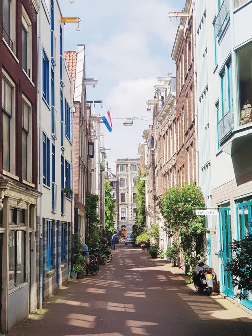 Free Cozy narrow street in Amsterdam featuring Dutch-style buildings and a flag on a sunny day. Stock Photo