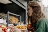 在户外市场，一位年轻女子正在挑选新鲜水果，她注重健康饮食和生活方式