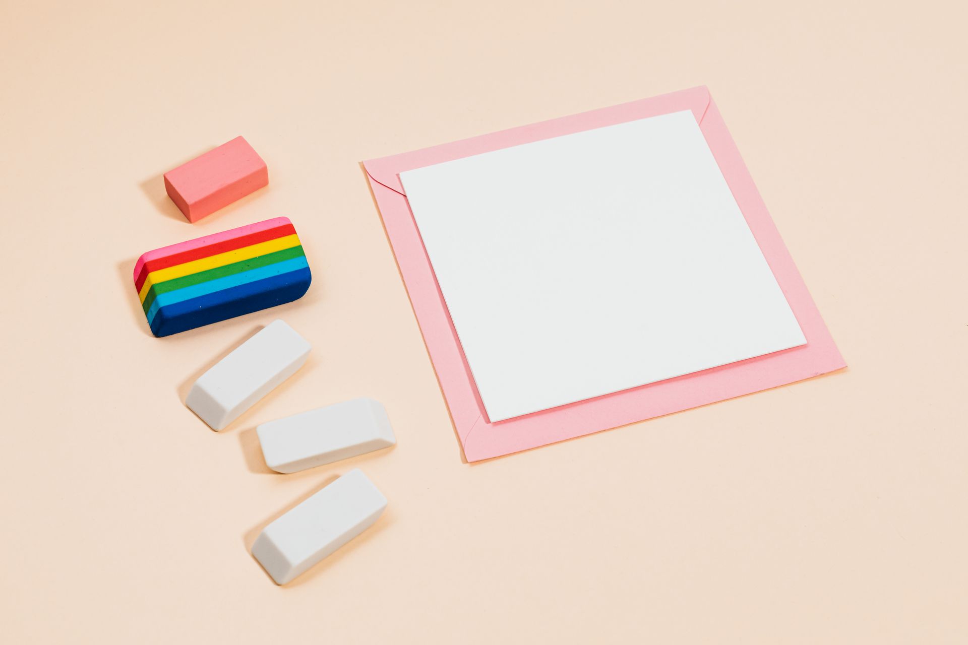 Flat lay of colorful erasers and a blank note on a soft pink background for stationery themes.