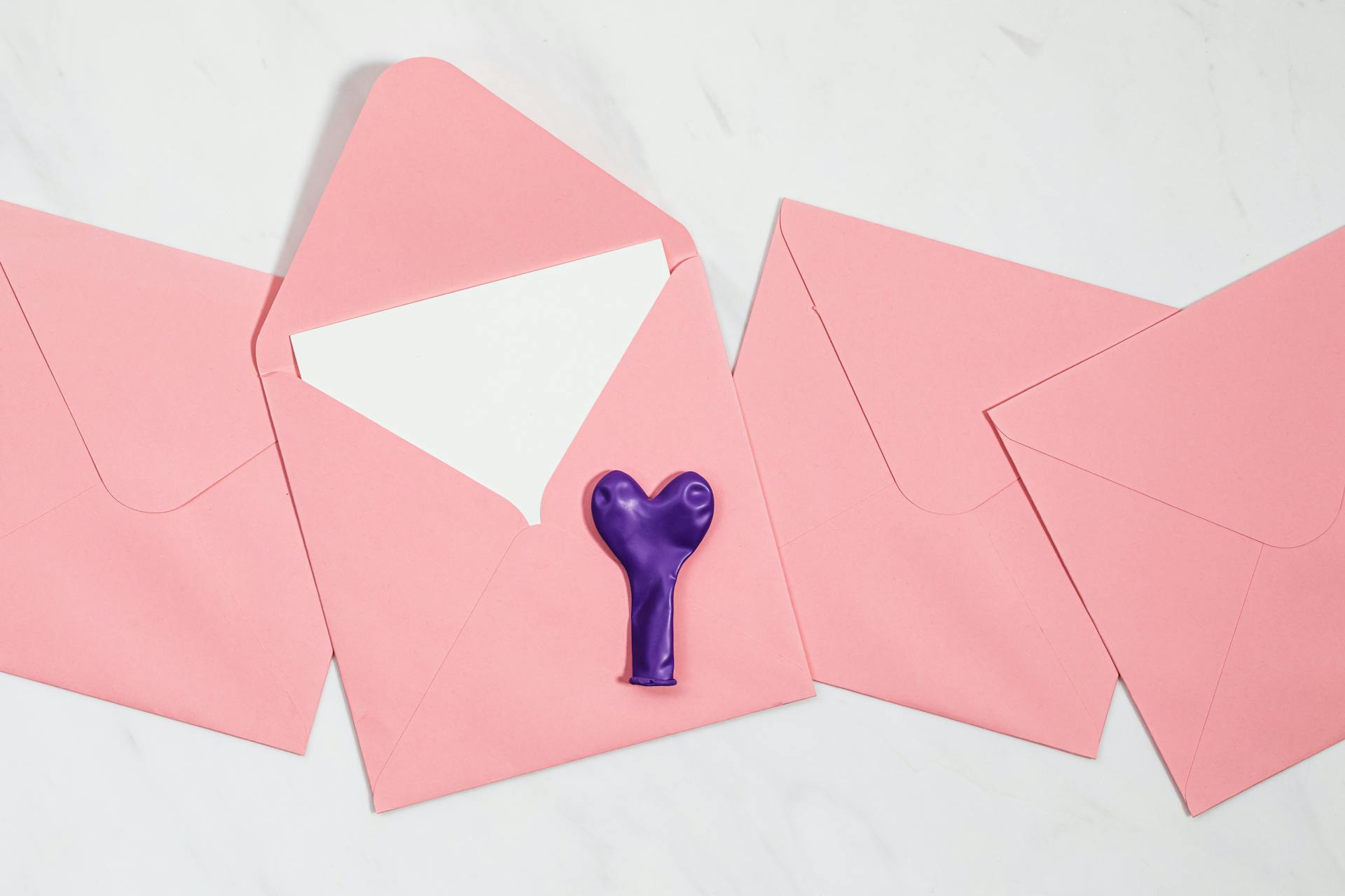 Pink envelopes with purple heart balloon on white background, offering a romantic, festive feel.